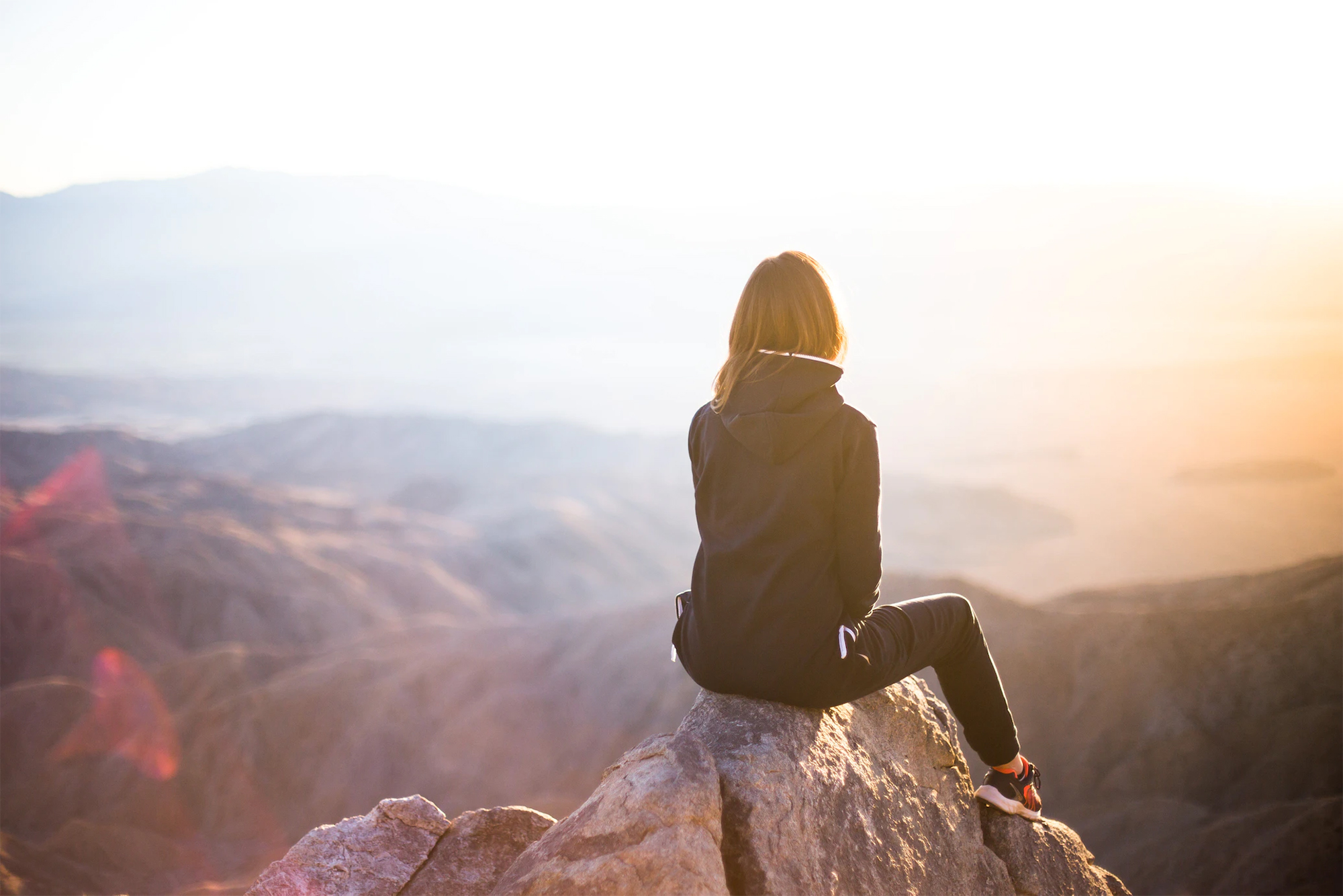 Girl on a hike sitting on the top of a mountain overlooking the mountain range and ocean