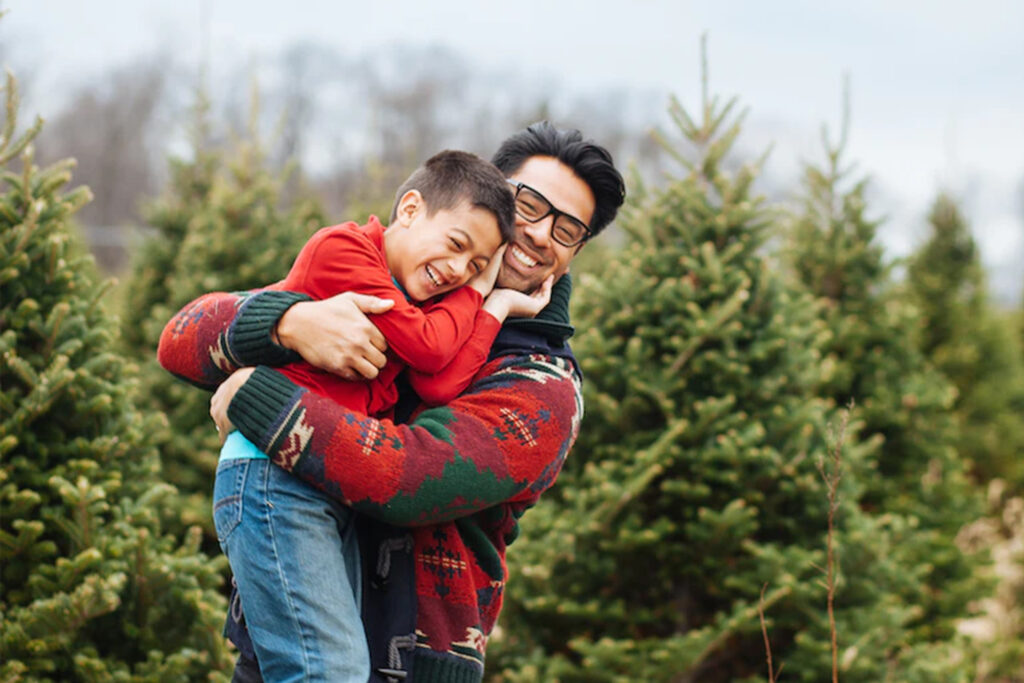 Father and son at the tree farm with green evergreen Christmas trees all around