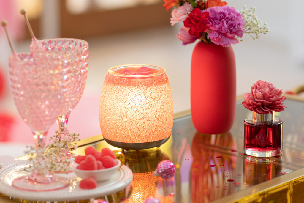 Fun love-inspired decor for Galentine's Day party with pink glasses, a pink vase with an assortment of pink flowers, the Pink Sunshine Dahlia Darling Fragrance Flower and a Pink Champagne Scentsy Wax Warmer