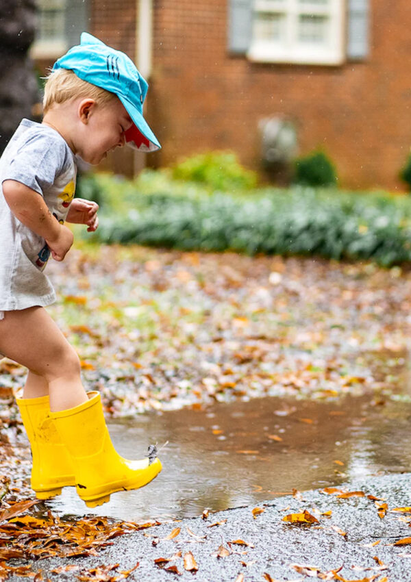 Kid with yellow rain boots jumping in a puddle