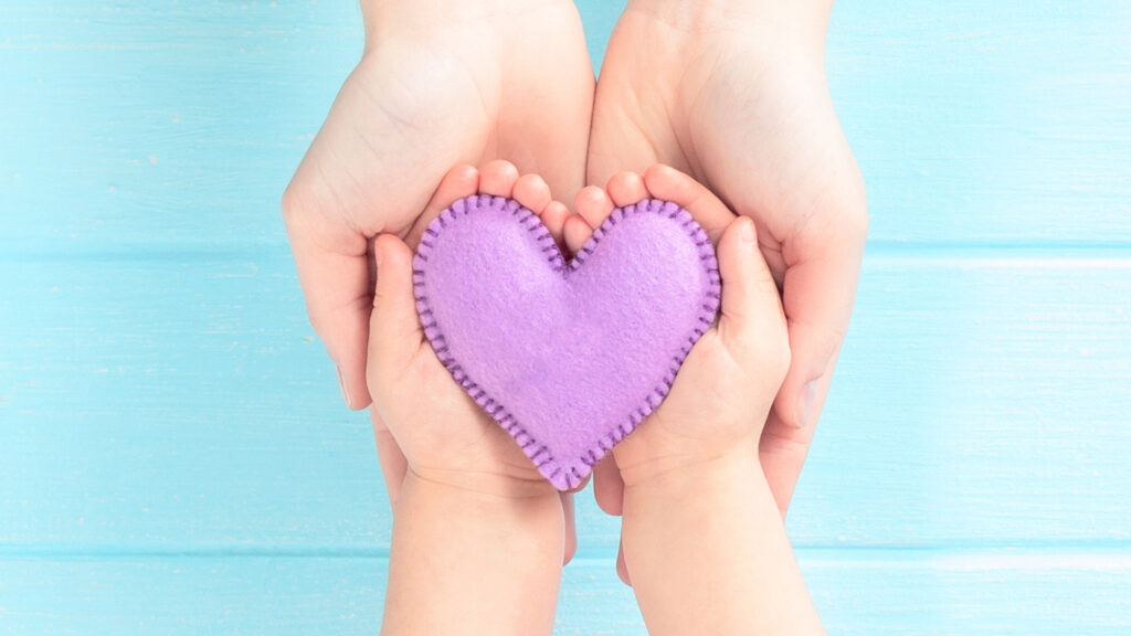 Adult and baby hands holding a purple fabric heart