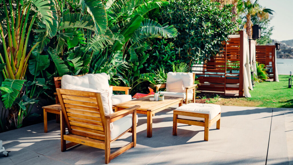 Outdoor Patio set with white cushions with big green leafy plants and cabanas nearby 