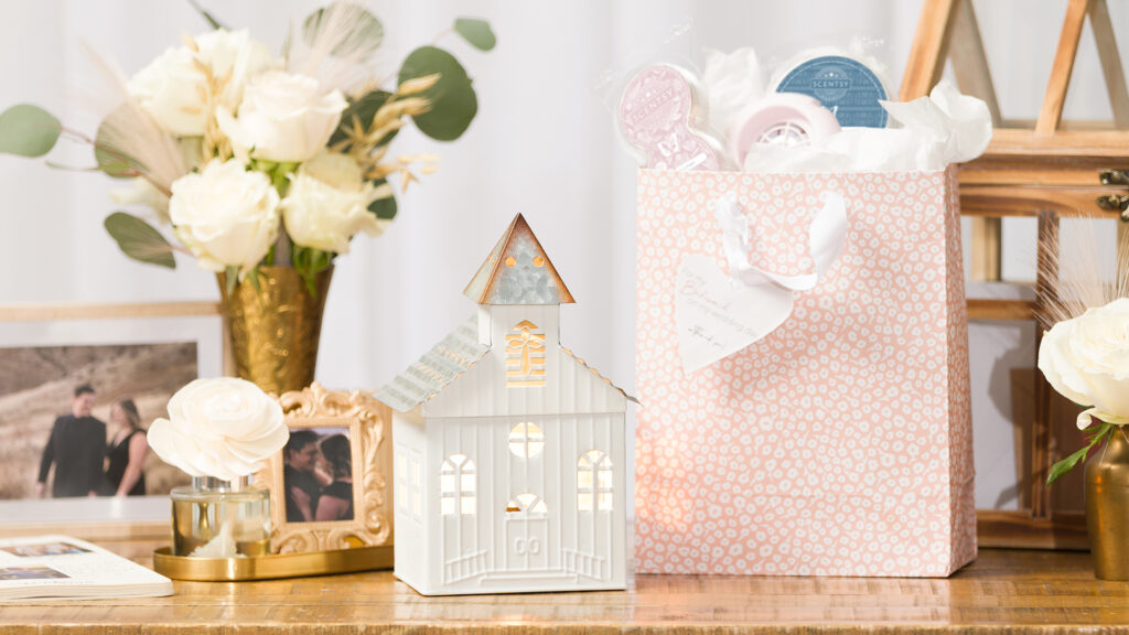 A pink wedding gift bag full of Scentsy products sitting on a table with photos, flowers, a wax warmer and fragrance flower