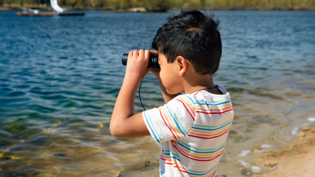 A young boy at the beach with binoculars looking at the water