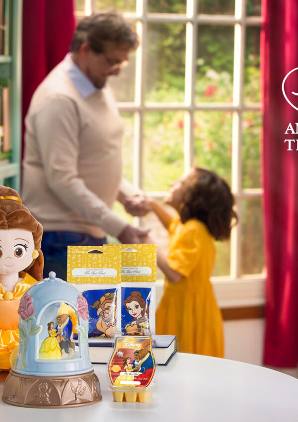 Disney Beauty and the Beast scent products from Scentsy sitting on a table with a father and his daughter dancing in the background wearing a Belle yellow dress