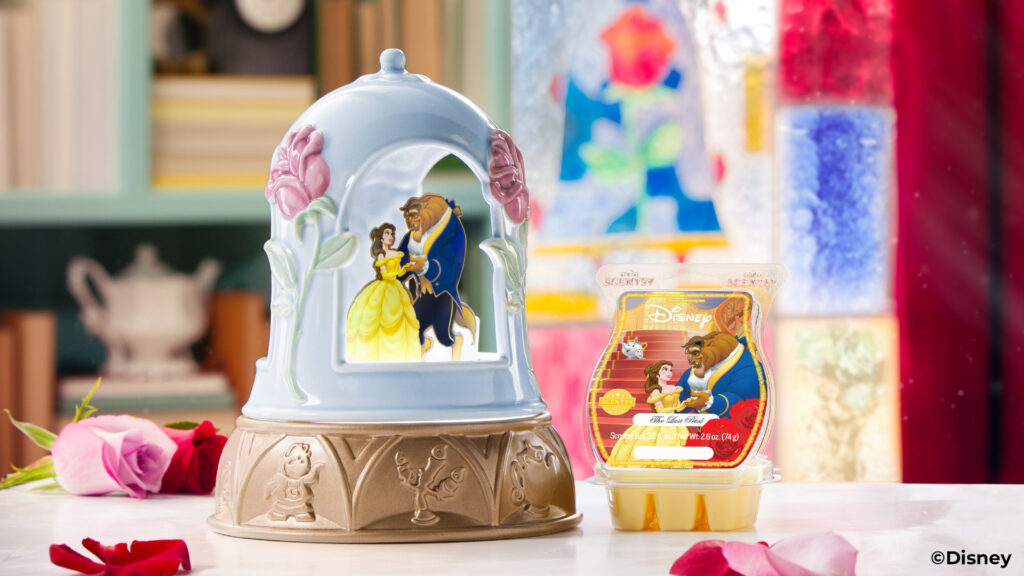 The Enchanted Love Wax Warmer and  The Last Petal scented wax bar from Disney Beauty and the Beast Collection sitting on a table beside roses, a teapot and a mosaic glass window