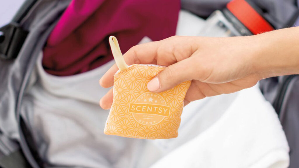 A woman's hand holding up an orange scentsy scent pack over a gym bag
