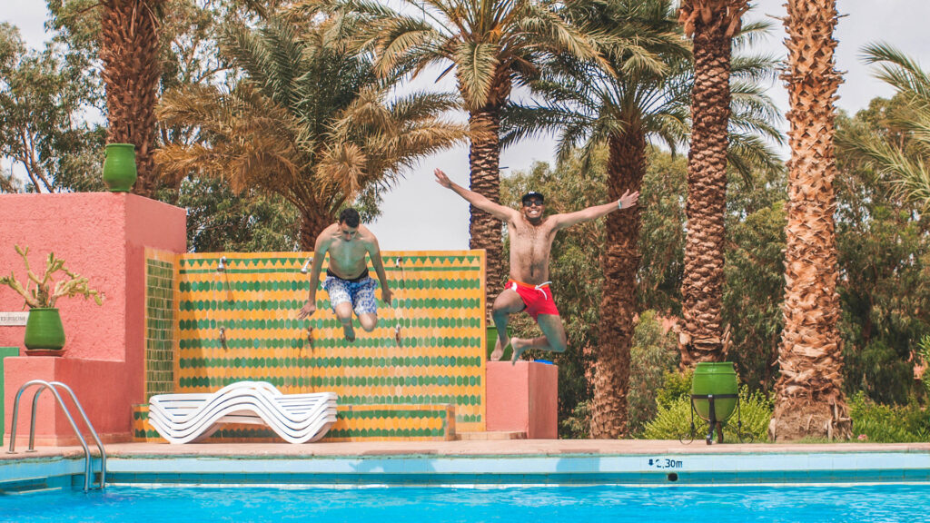 Two teenage boys jumping into a pool with palm trees around enjoying summer