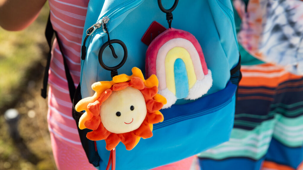 A kid on a summer bike ride with a Ray & Sunshine buddy clip and Happy Thought buddy clip on their light blue back pack