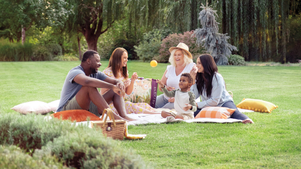 A family making memories on a summer park picnic with a child throwing an orange fruit