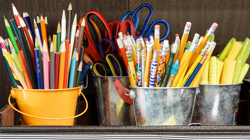 Four small, neatly organized tins holding colored pencils, scissors, pencils and highlighters