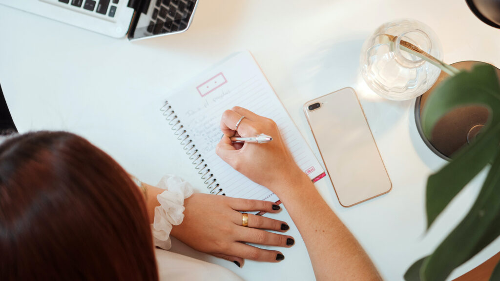 A girl sitting down at her desk writing down her homework to do list on a notepad