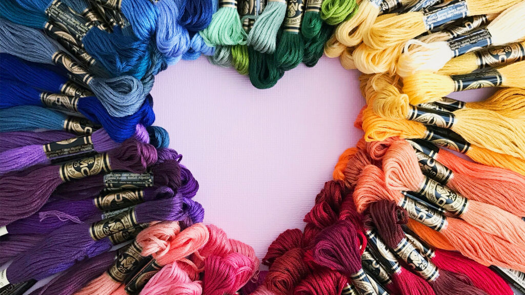 A bunch of fabric string in all different colors of the rainbow arranged to make a heart shape