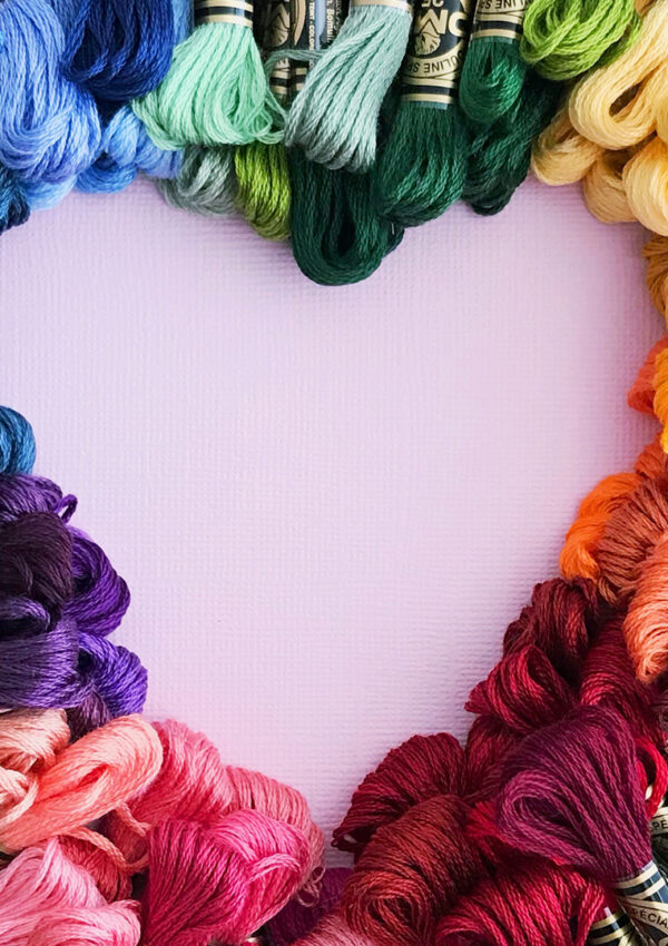 A bunch of fabric string in all different colors of the rainbow arranged to make a heart shape