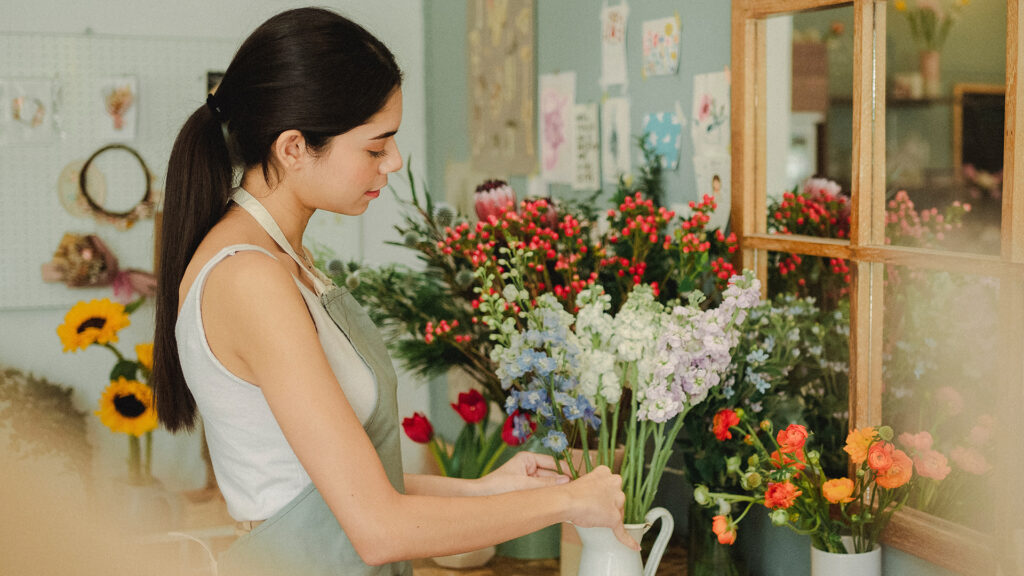 A woman putting together a floral arrangement in a white case
