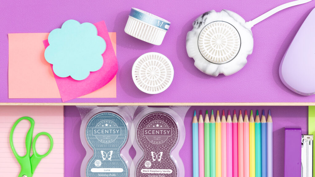 Scentsy mini fan diffuser with scentsy pods scented in luna and black raspberry vanilla fragrance sitting on a school desk beside school supplies to make your dorm feel like home