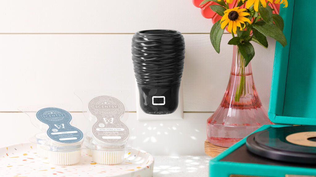 Scentsy wall fan diffuser with scentsy pods sitting on a side table in a dorm beside a vase of flowers and teal record player