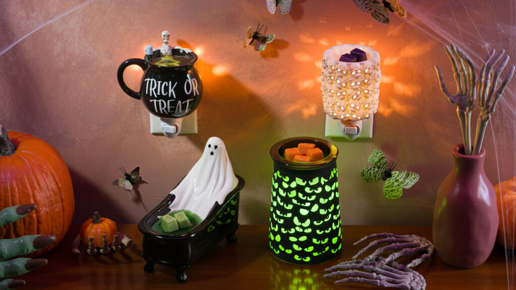 A collection of Halloween themed Scentsy warmers and mini warms glowing together on a shelf with seasonal decor.