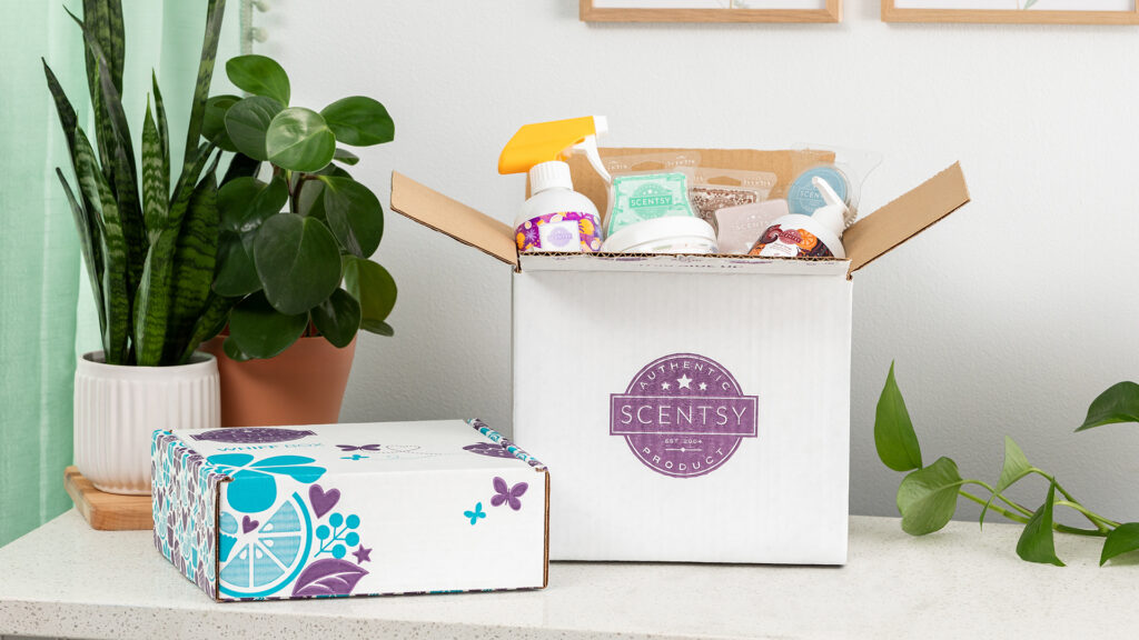 A scentsy club subscription opened at a home on a table with the box full of scent products beside green house plants