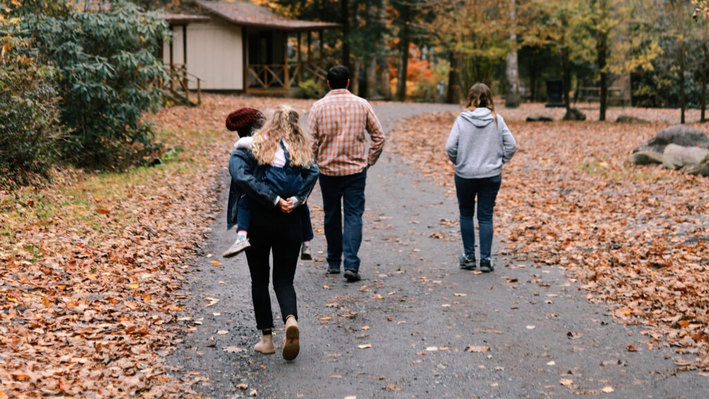 A family of four on a nature walk in fall with orange leaves falling all around