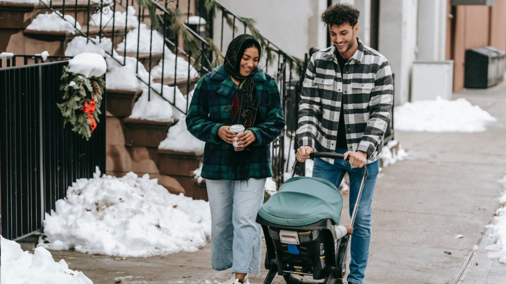 A couple on a walk pushing their baby in a stroller on a snowy sidewalk