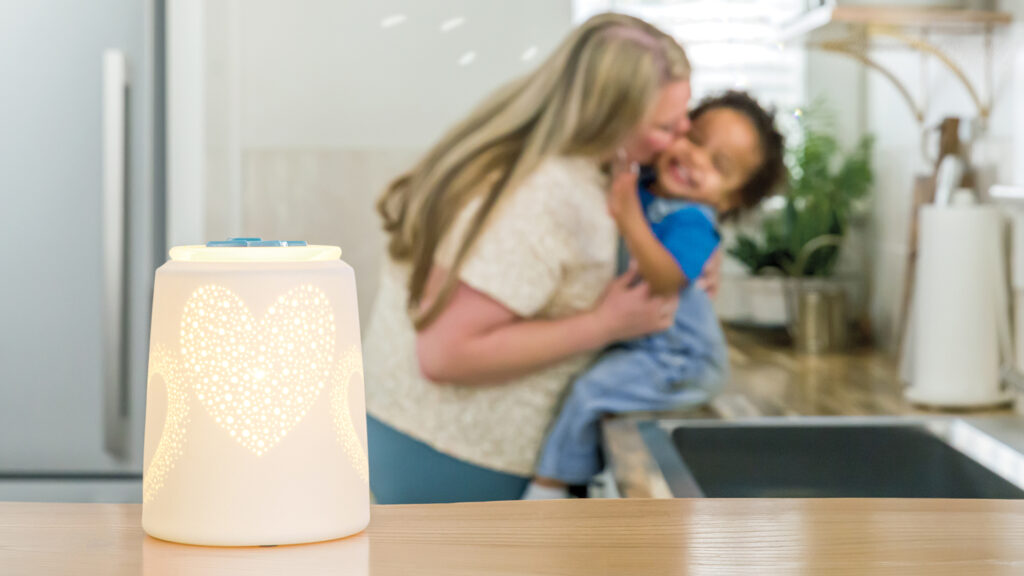 Scentsy heart to heart wax warmer lit up and melting blue wax cubes with a  mother holding her son and kissing his cheek in the background