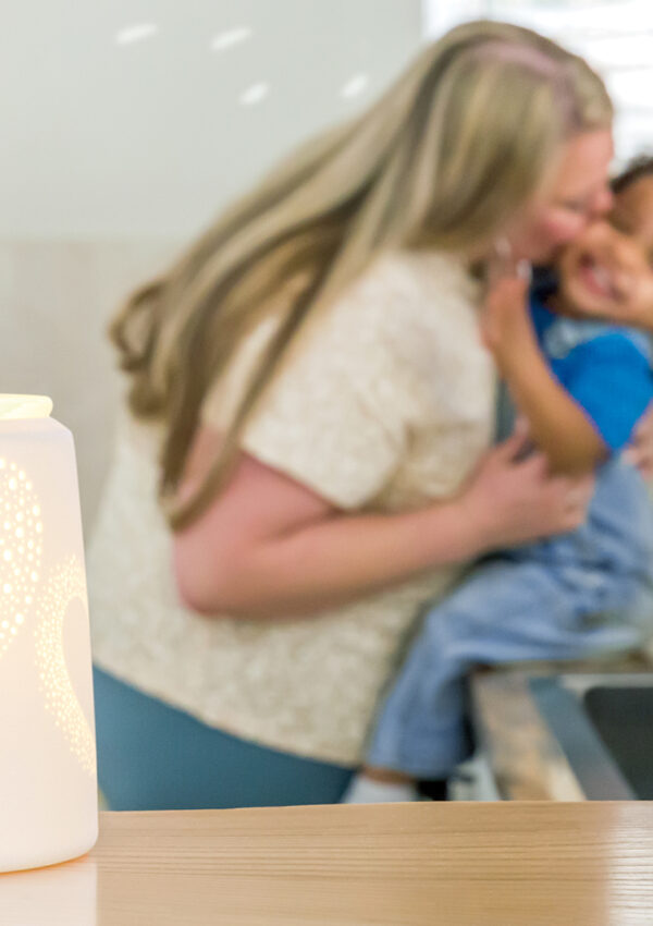 Scentsy heart to heart wax warmer lit up and melting blue wax cubes with a mother holding her son and kissing his cheek in the background