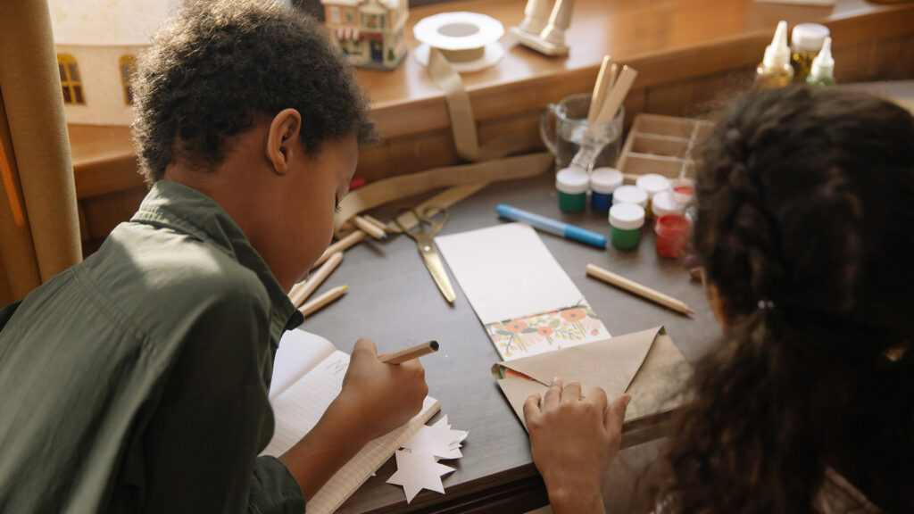 Two kids writing letters and crafting and putting them in envelopes
