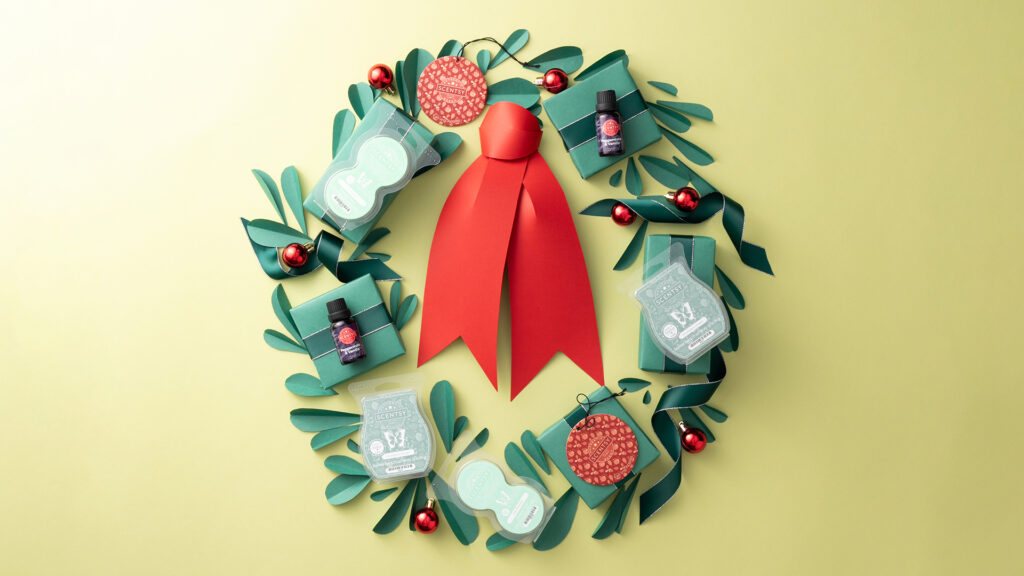 a green paper wreath with a red bow with scentsy products scattered around in the branches
