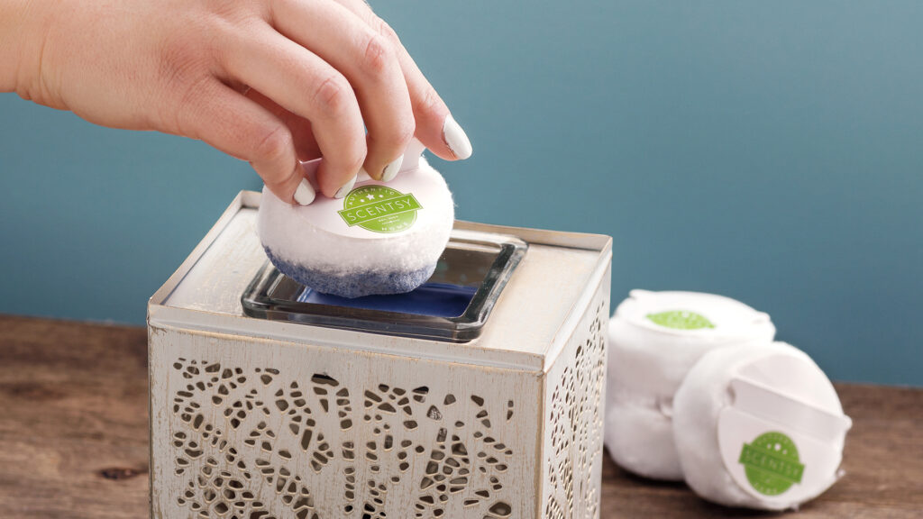 Scentsy cotton pad clean up being dipped into melted wax in a wax warmer to absorb the dark blue wax