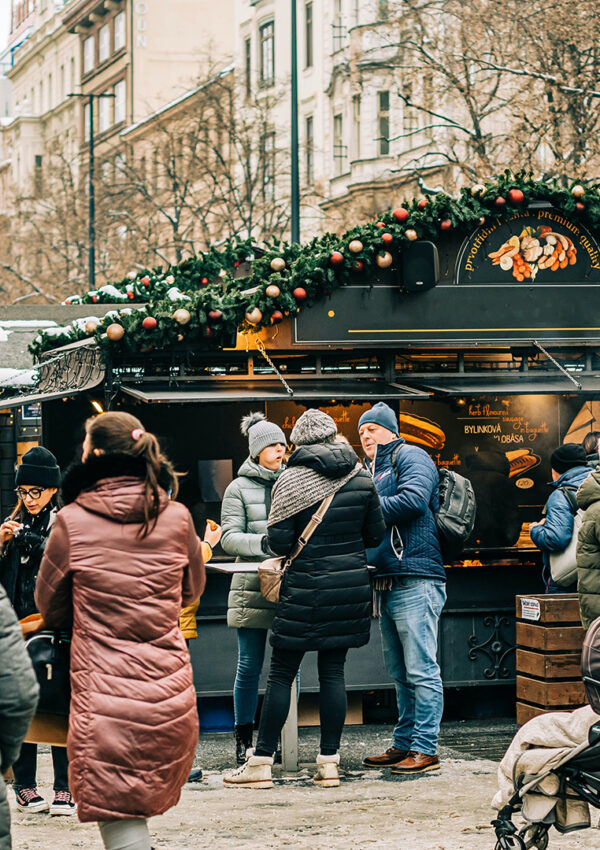 Photo of people at an outdoor holiday market with trees and a food stand decorated in ornaments and garland