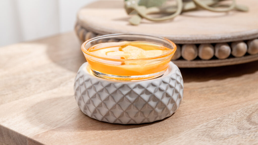 Scentsy simply diamond wax warmer with melted orange wax sitting on a side table next to a pair of glasses