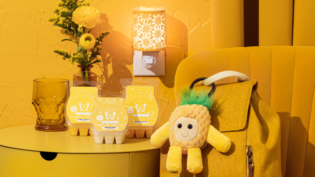 scentsy products that are yellow including wax bars, yellow floral mini wax warmer, and pineapple backpack clip hooked to a yellow backpack in a yellow room