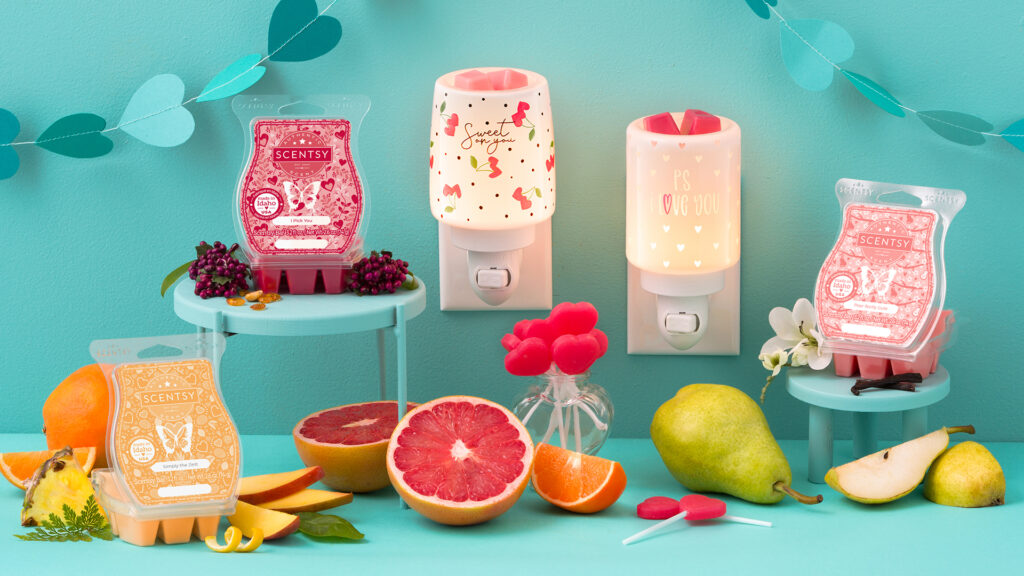 The Cherry Picked Mini wax Warmer and Sweet Sentiments Mini wax Warmer plugged into the wall melting red and pink wax cubes with three wax bars beside them and their scent notes scattered beside the bars
