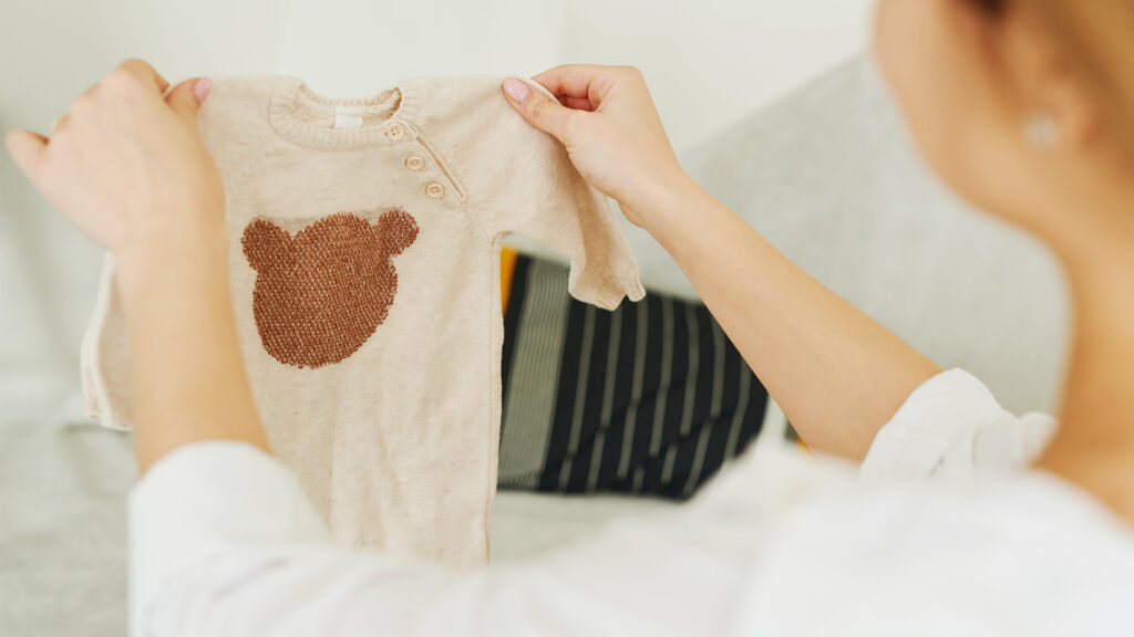 a woman holding up a baby onsie that is light brown with a darker brown bear head on the front and 3 buttons