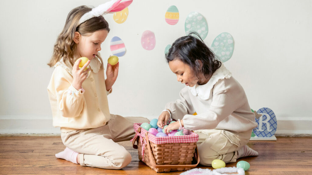 Two children one with bunny ears on and the other digging through an easter basket full colorful plastic easter eggs 