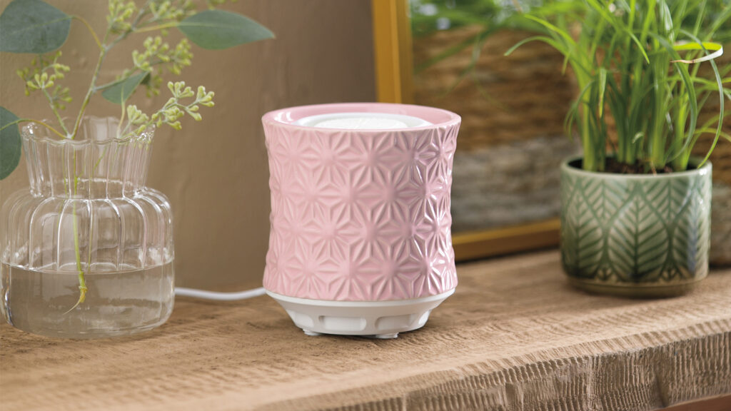 A pink tabletop fan diffuser sitting on an entry table in the middle of a vase of flowers and a potted plant