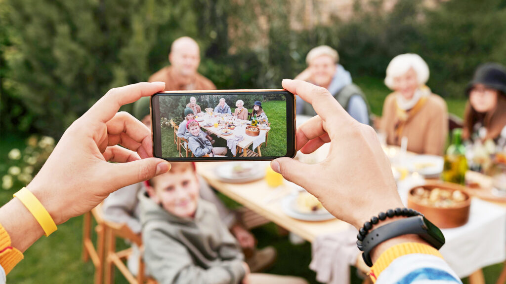A person holding a phone taking a photo of their family sitting at an outdoor table