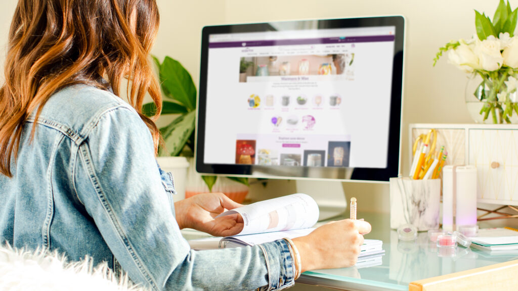 A woman sitting at her computer on her desk writing in a planner