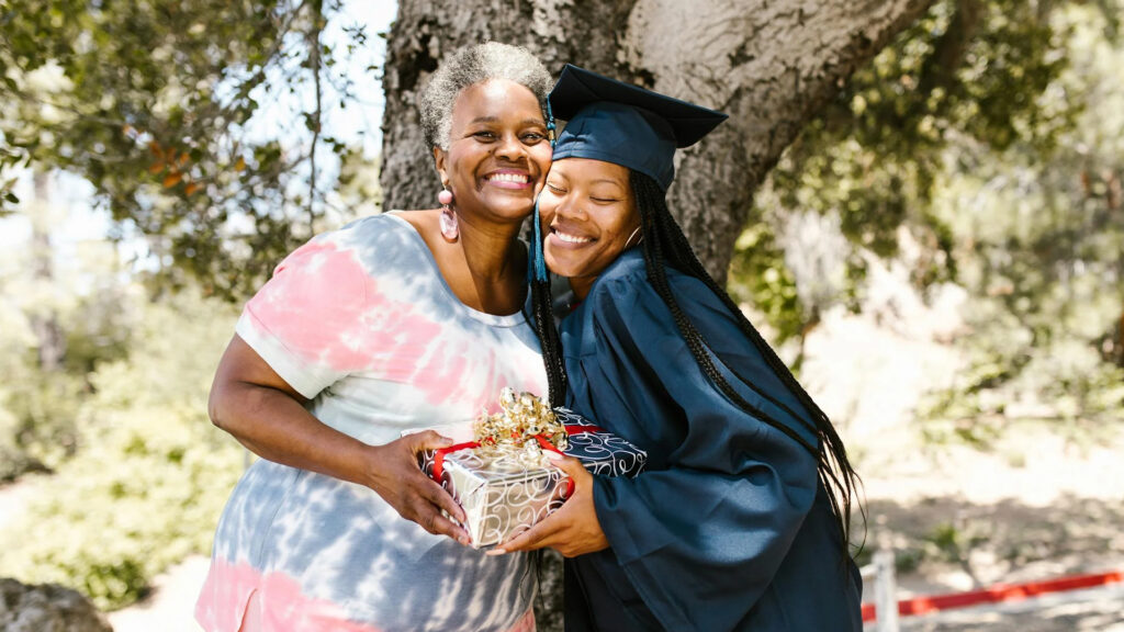 A girl who is a graduate and her mom smiling for a picture holding onto a graduation gift