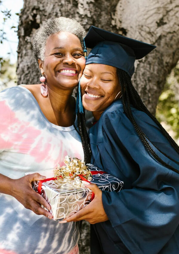 A girl who is a graduate and her mom smiling for a picture holding onto a graduation gift