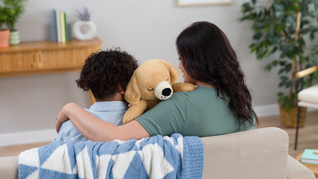 A mother and her son sitting on a couch cuddling the Truman the Terrier Scentsy Weighted Buddy.