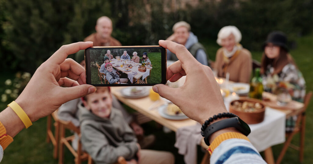 When family gathers for a reunion use Scentsy's tips to make the most of the event. In this image, a person takes a digital photo of people gathered at a picnic table.