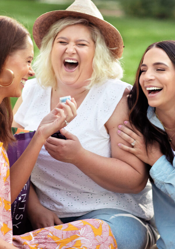 Three women outdoors sampling a Scentsy Fragrance tester and laughing together