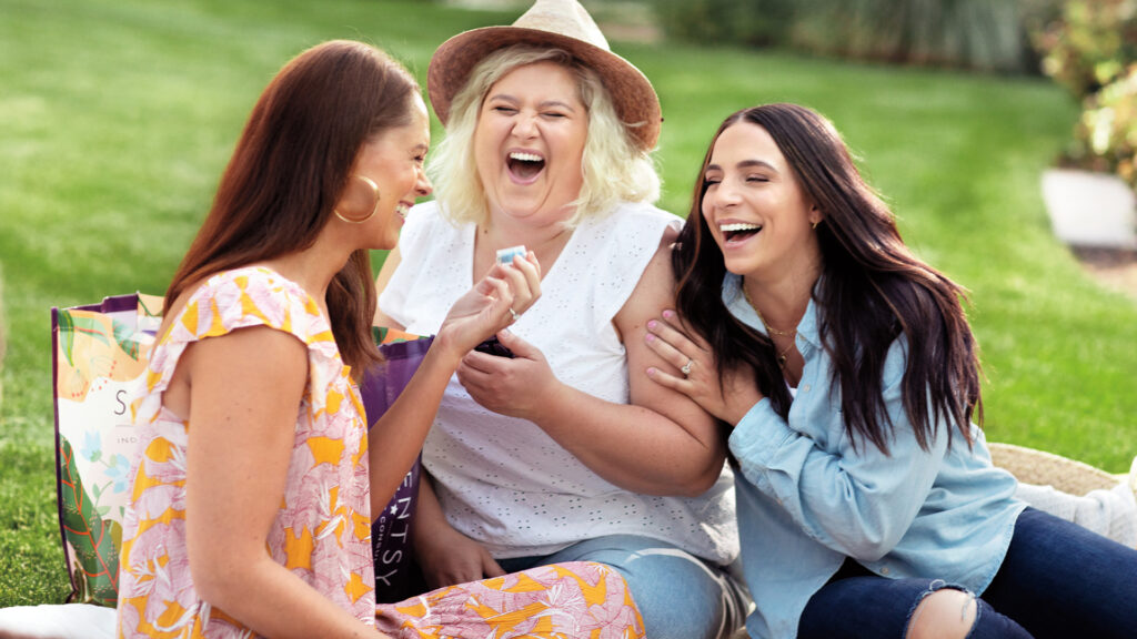 Three woman at a fragrance party laugh together as they smell a Scentsy wax fragrance sample.