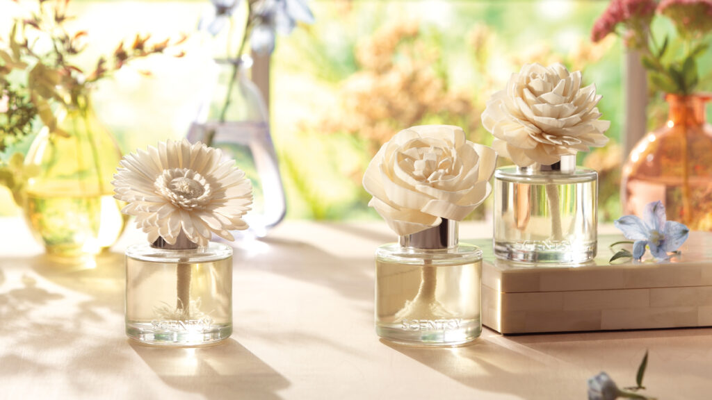 Three Scentsy fragrance flowers displayed on a table among other floral arrangements.