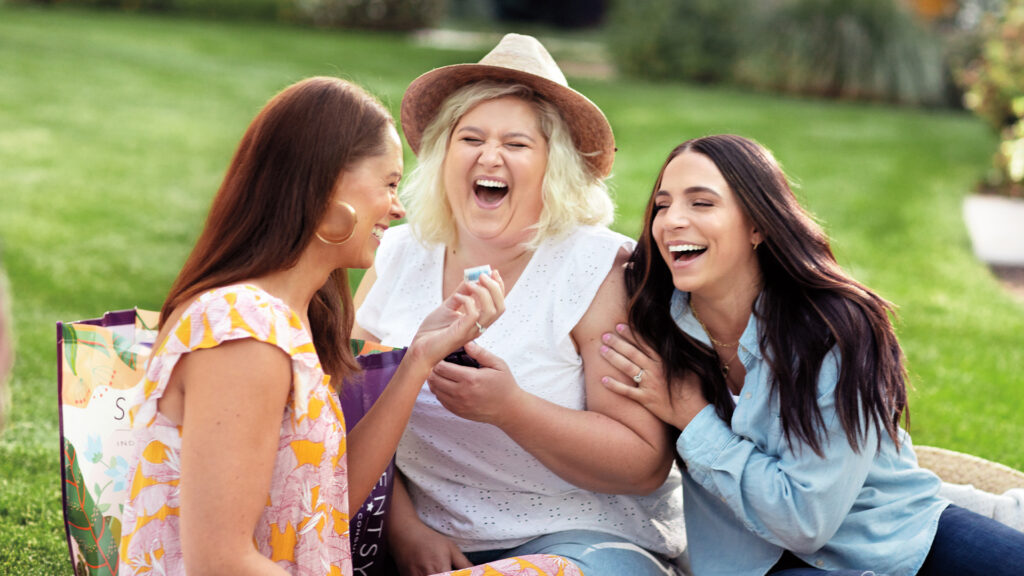 Three women laughing together as they smell a Scentsy wax bar.