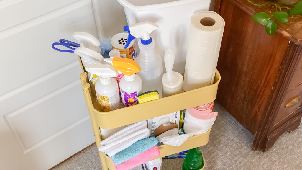 A DIY Cleaning Cart loaded with different cleaning supplies such a paper towels, bleach, Scentsy cleaning products, brushes, towels, and trash bags.