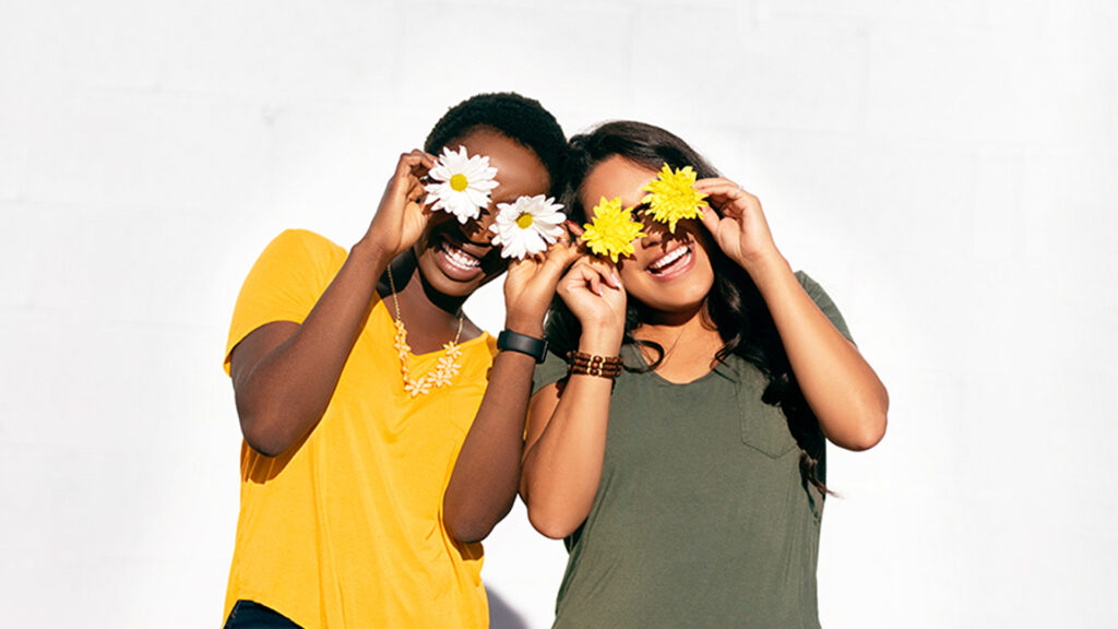 Two people pose for a photo, smiling and with flower blossoms placed over their eyes.