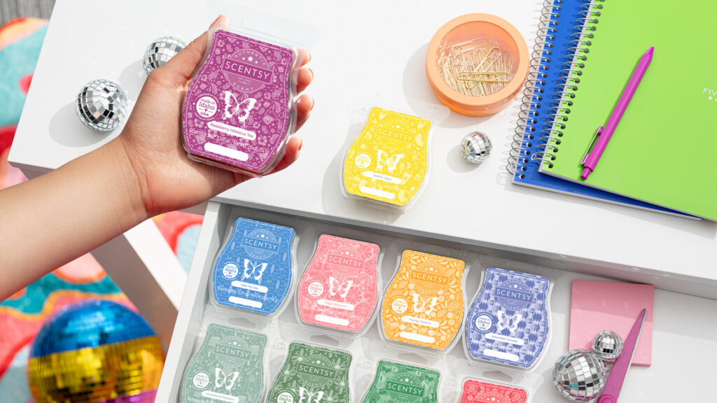A hand holding a Scentsy wax bar with an assortment of more wax bars in the background, all placed within the drawer of a perfectly organized desk.